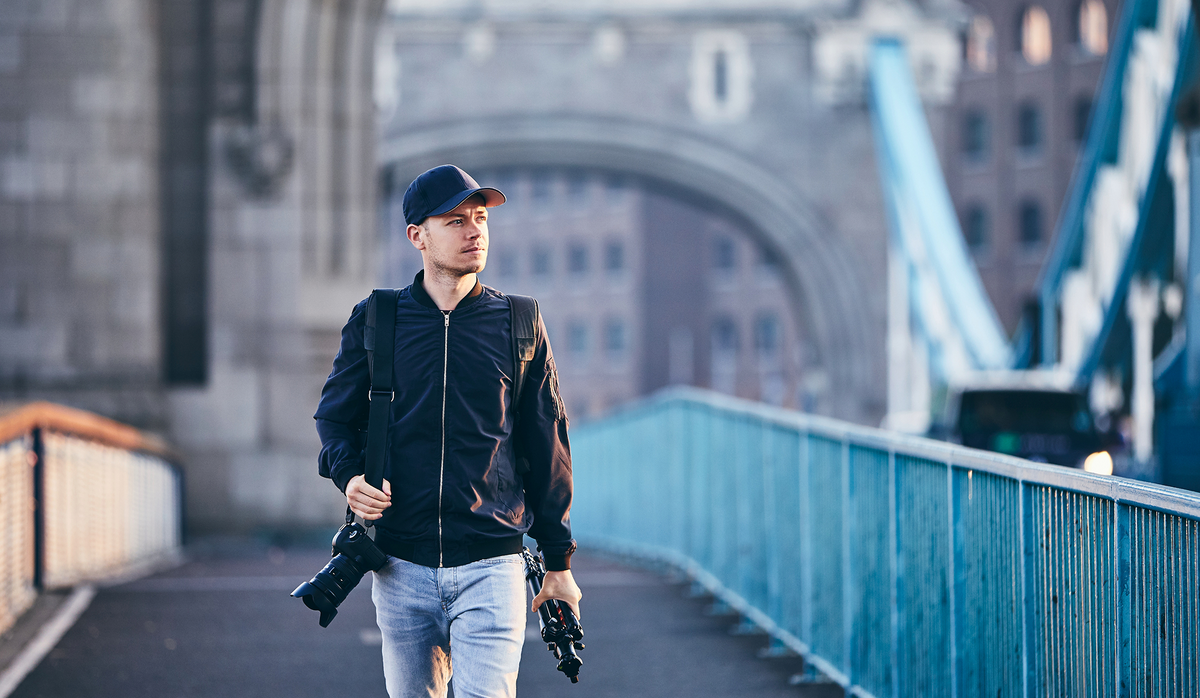 Photographer walking across Tower Bridge with a camera and tripod.